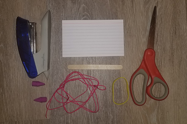 a stapler, index card, scissors, popsicle stick, rubber band, string, and eraser caps