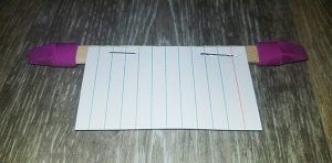 an index card stapled to a popsicle stick with eraser caps on the ends