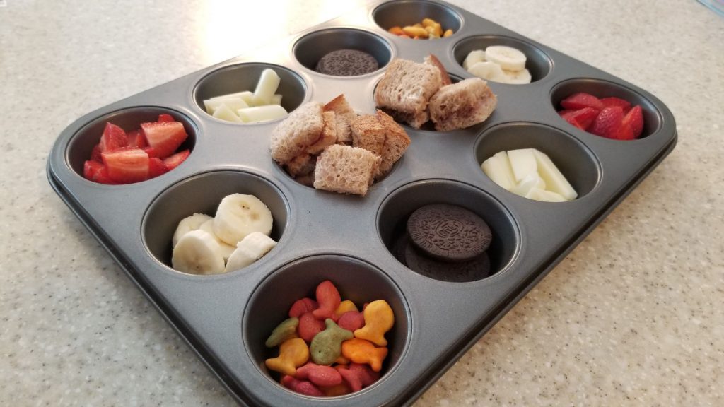 A muffin tin filled with an assortment of bite-sized snacks