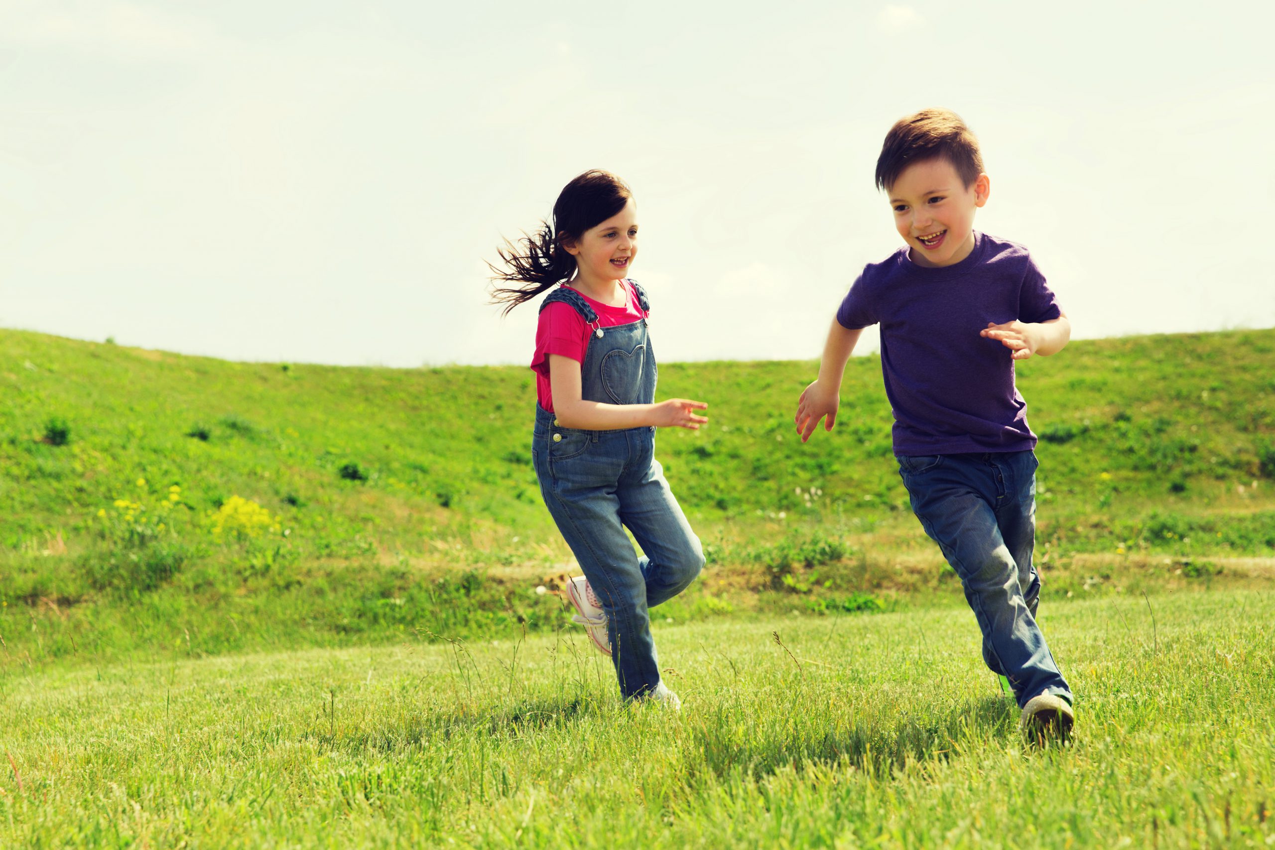 a boy and girl running in a large green field