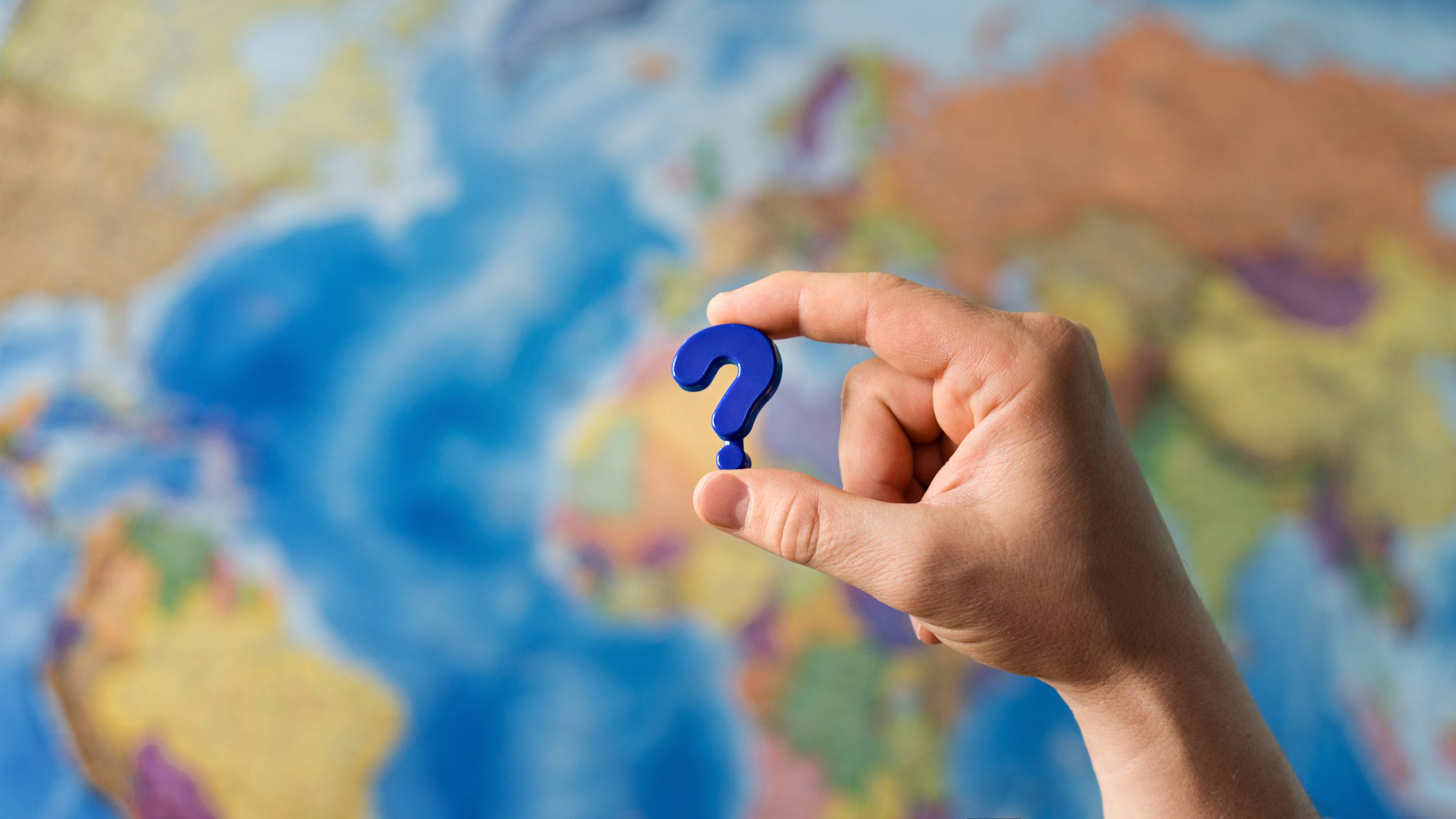 Adult hand holding question mark plastic toy on the world political map background.
