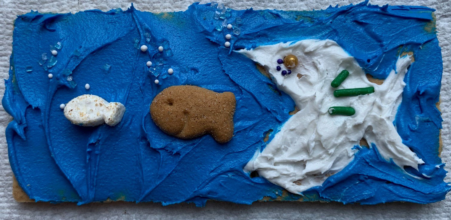 Graham cracker snack with fish made out of icing trying to eat another fish made out of S'mores goldfish
