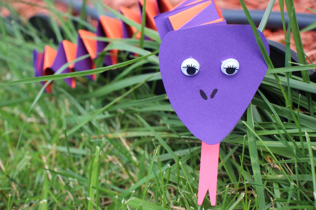A purple and orange snake made out of construction paper rests on green grass