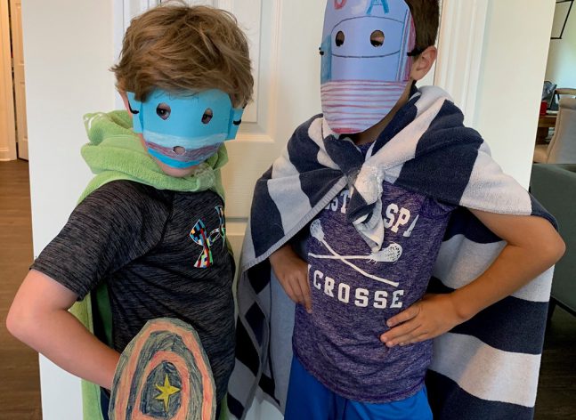 Two children posing with superhero masks, towels for capes and a shield