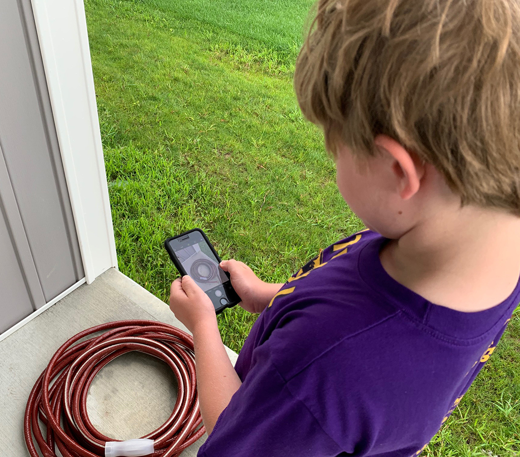 Child taking a picture of a hose shaped like the letter "O" with a smart phone