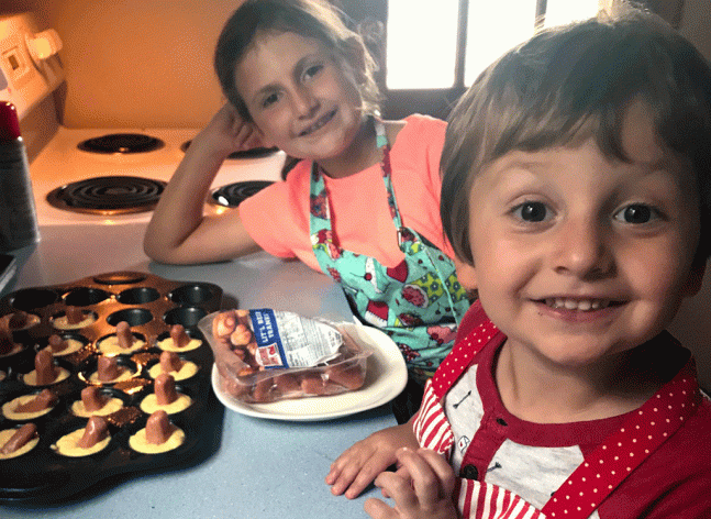 Two children smile at camera with hot dog mini corn muffins next to them on the table