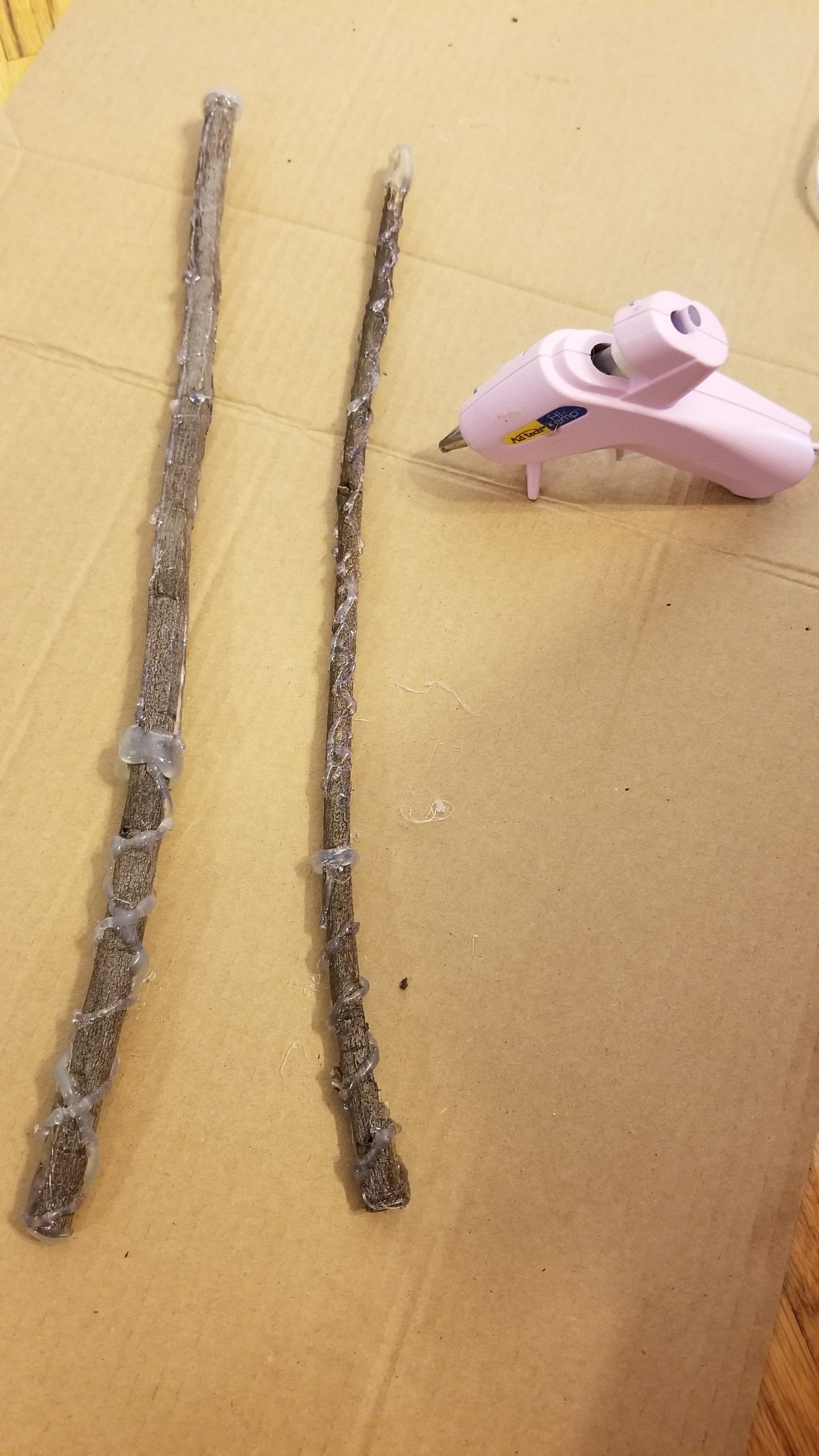 sticks laying on a piece of cardboard with hot glue on them and a hot glue gun next to them