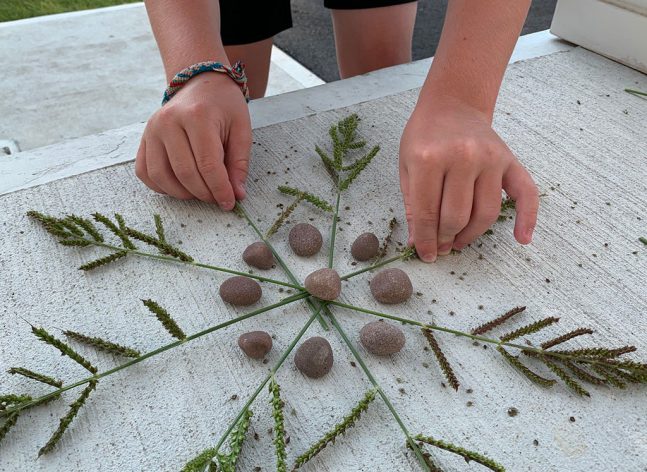 Child's hands creating a Nature Mandala with grass and rocks