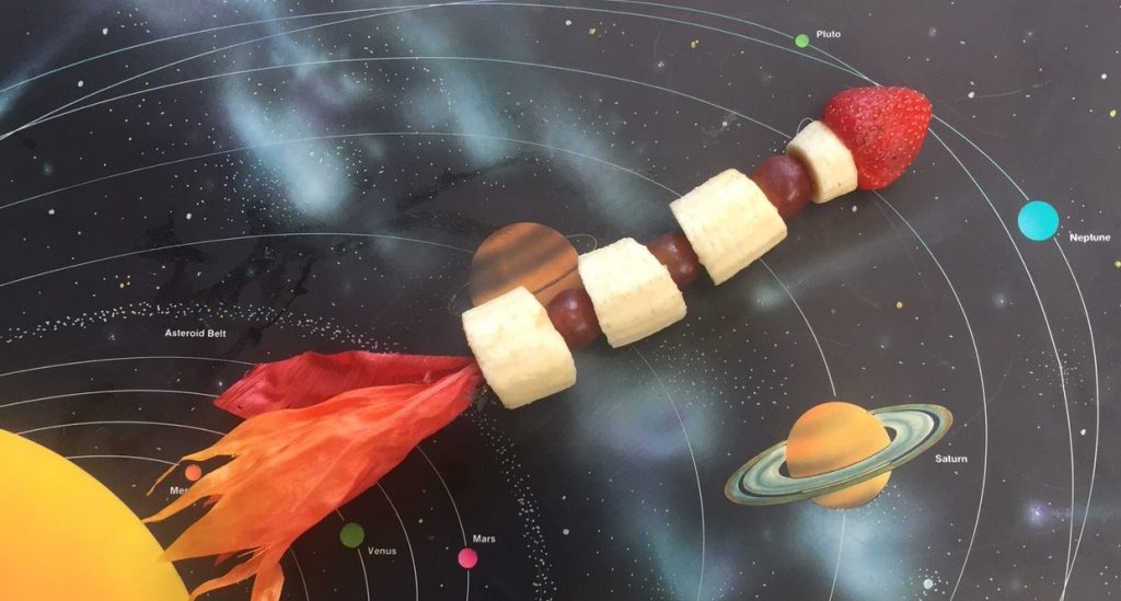 Bananas, grapes and a strawberry on a skewer to form a fruit kabob against an outer-space background
