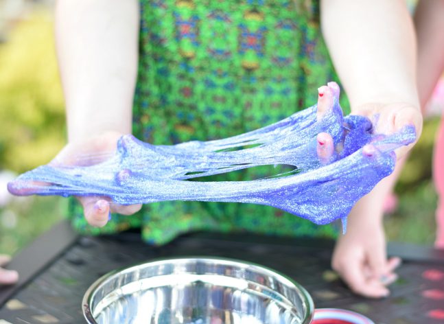 A child spreads purple slime between her hands
